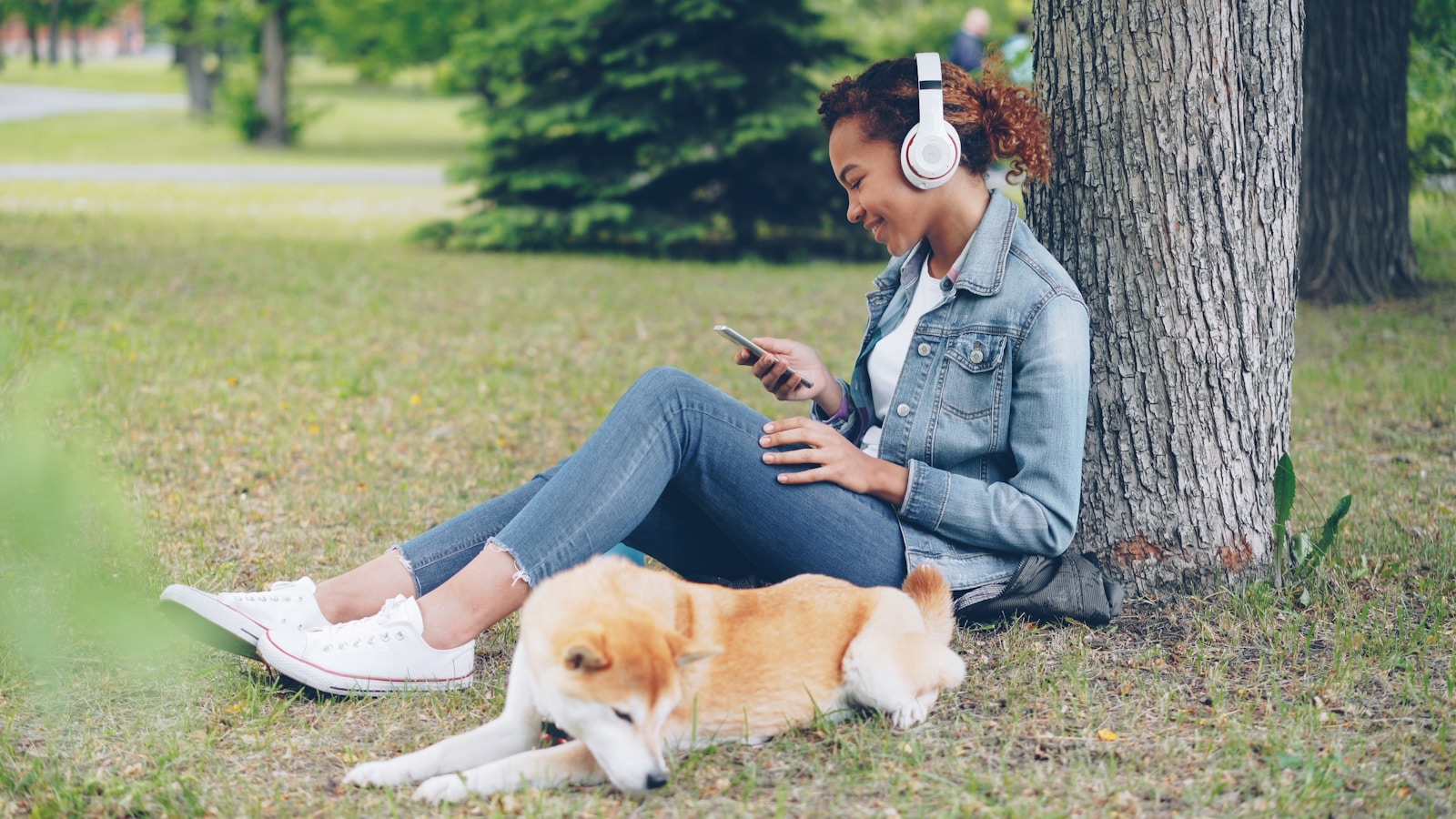 Woman enjoys music in the park with her dog.