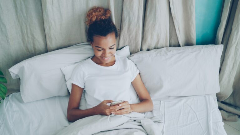 Young woman in bed looking at her phone.