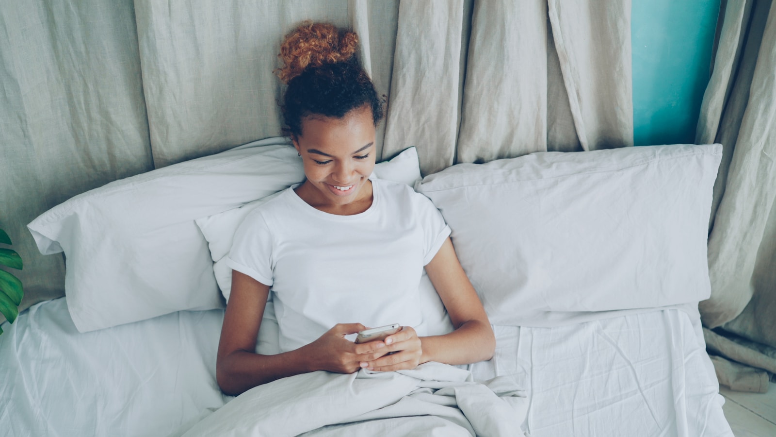 Young woman in bed looking at her phone.