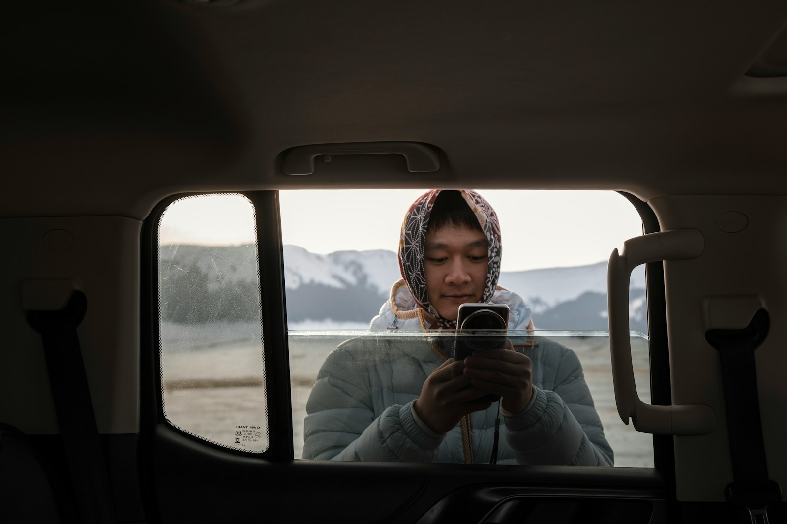 Person using phone in car with snowy mountains outside