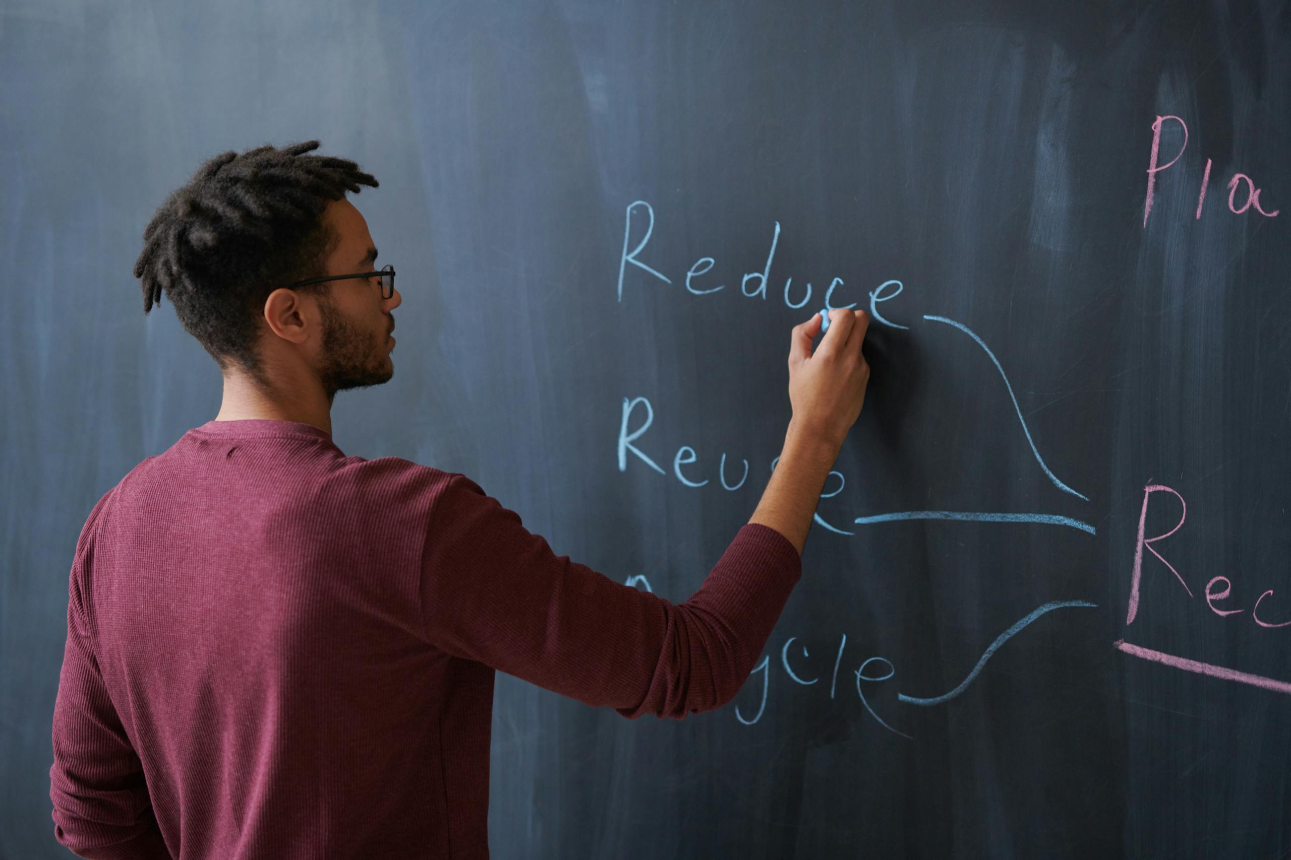 A person writes the words reduce, reuse, and recycle on a blackboard, promoting sustainability.