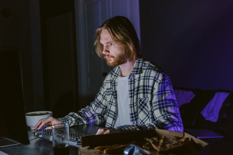 Young man intensely gaming on a computer in a dimly lit room at night.