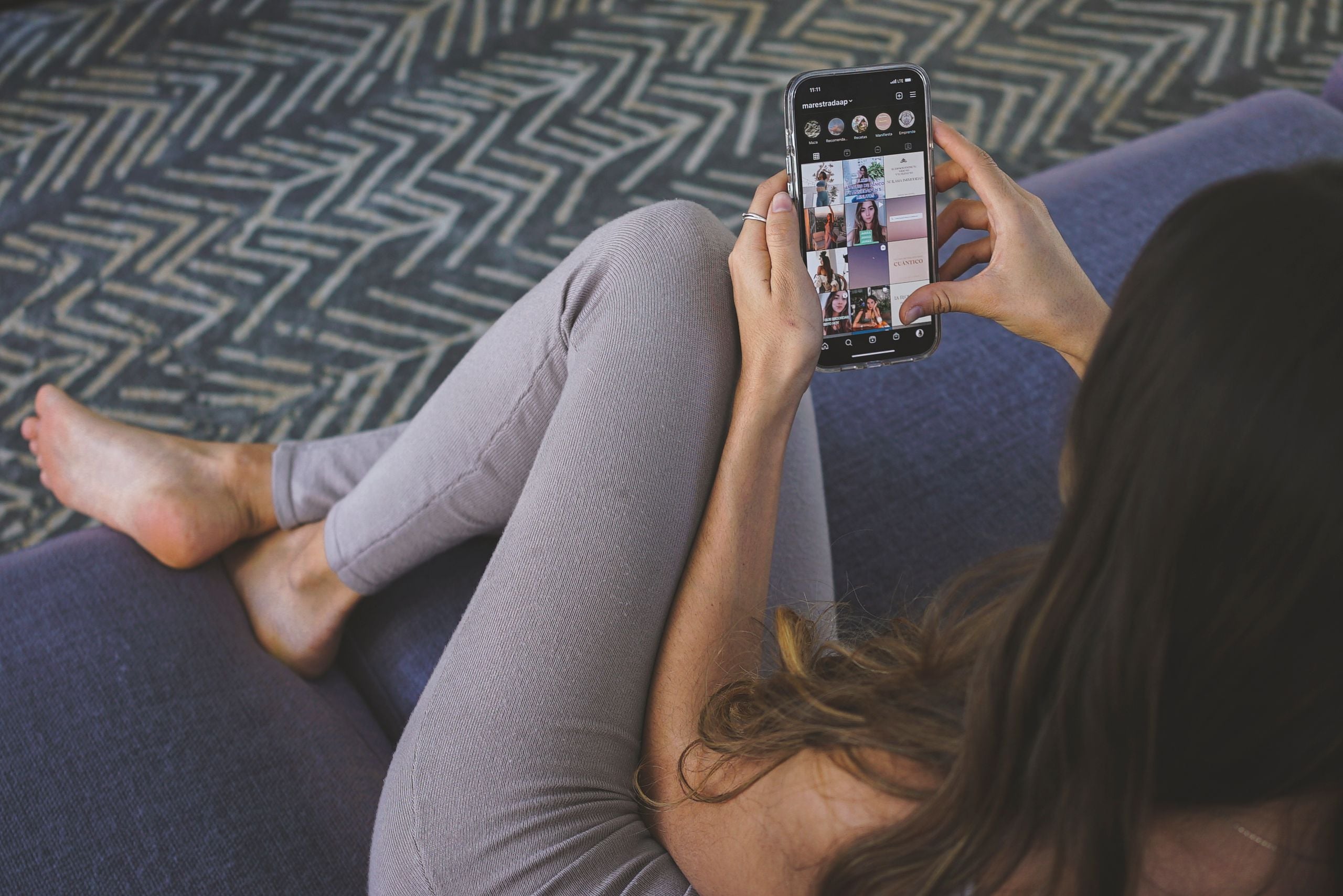 A woman relaxing on a sofa, engaging with social media on her smartphone. Modern lifestyle concept.