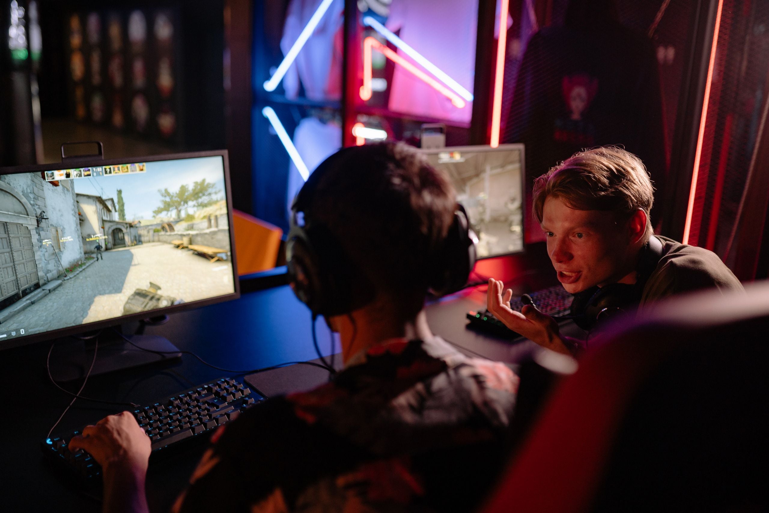Two gamers engaged in a heated video game session surrounded by neon lights and computer screens.