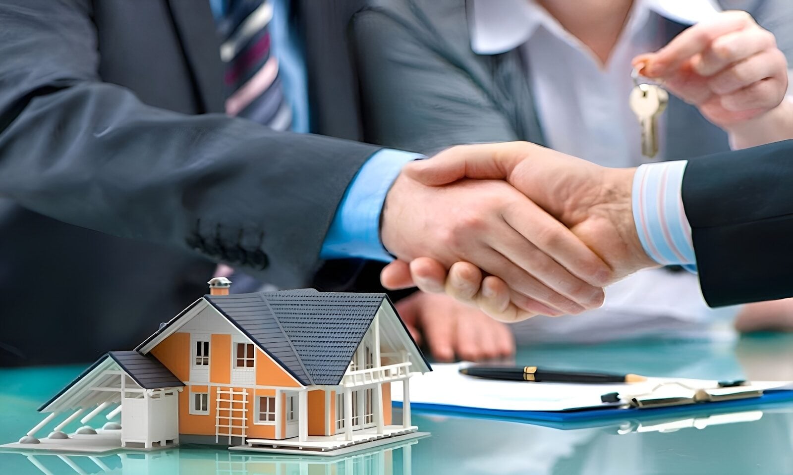 Two men shaking hands over a house model and keys.