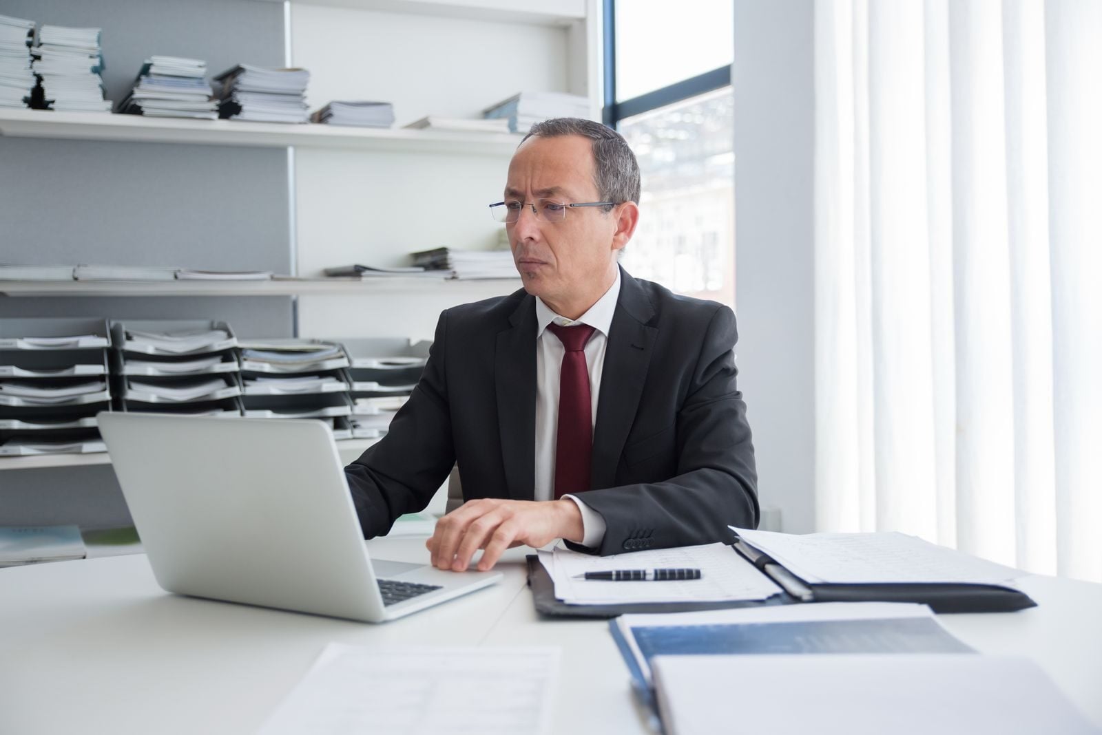 Focused businessman in a suit working at his office desk with a laptop and documents.